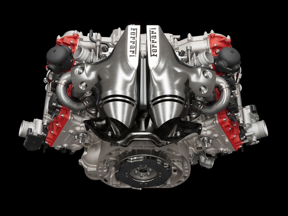 A high-performance Ferrari engine with silver metal intake manifolds prominently displayed, against a black background.