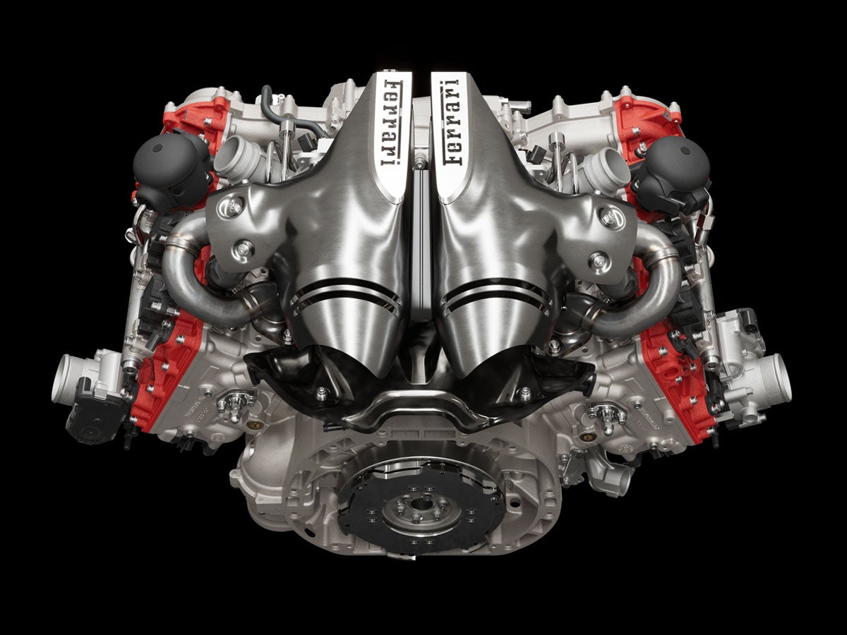 A Ferrari V8 engine, with shiny silver intake manifolds, red valve covers, and a black background.