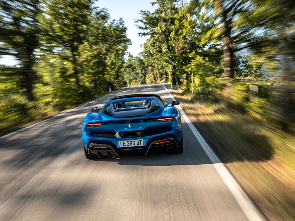 Rear view of a blue sports car speeding down a tree-lined road, motion blur implying high speed.