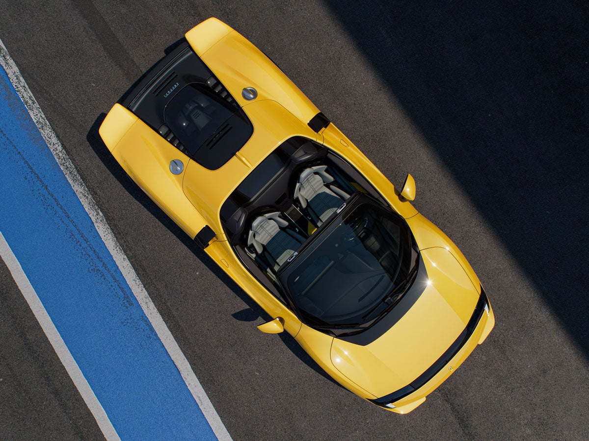 Aerial view of a bright yellow convertible sports car on a race track with blue and white markings.
