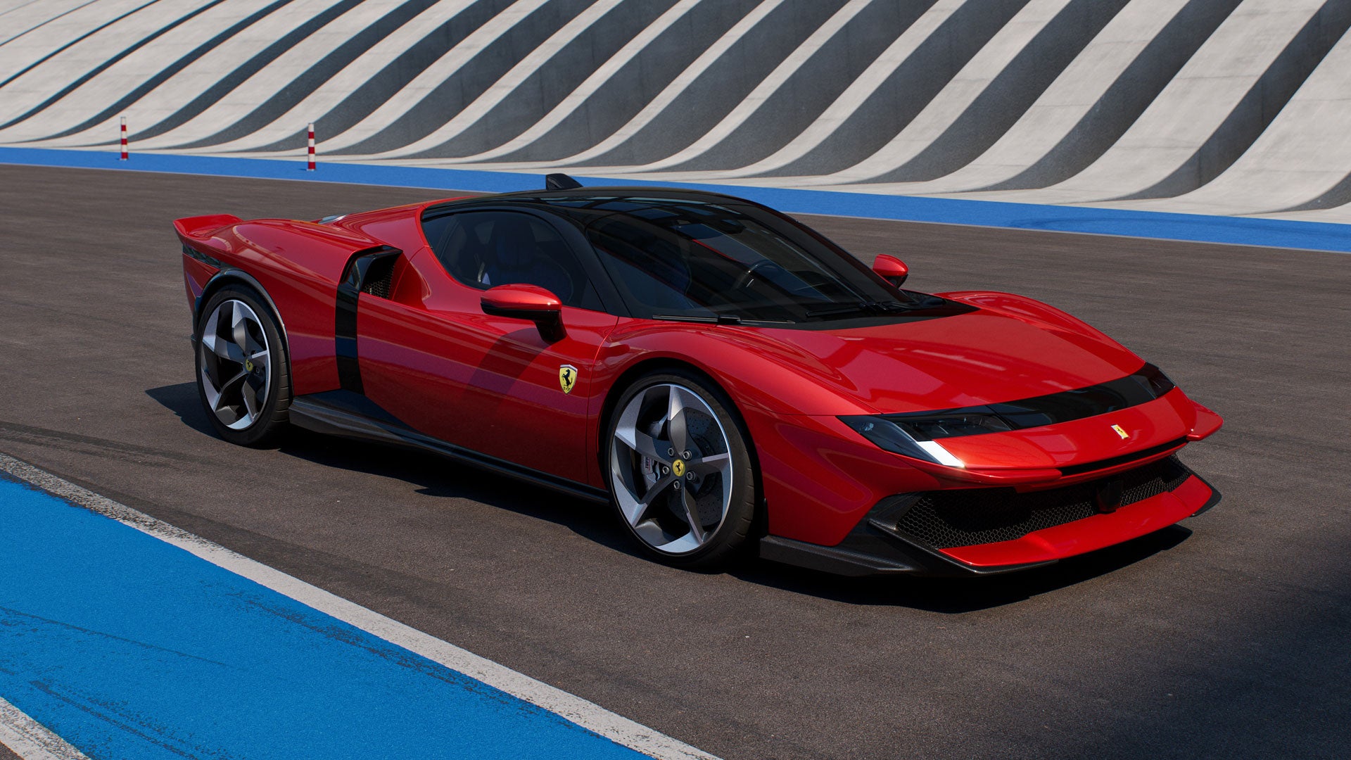 A sleek red sports car with a black roof is parked on an asphalt track, with a blue line and a striped wall in the background.