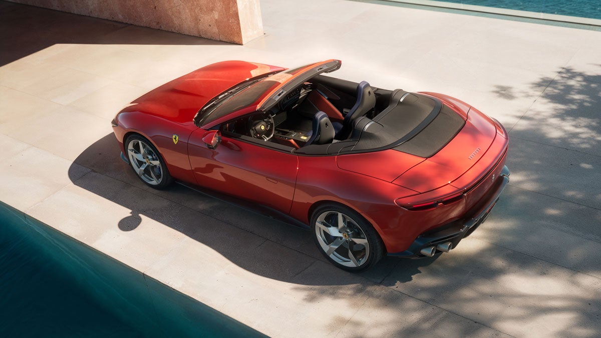 Red Ferrari Roma Spider convertible parked on stone patio beside a pool with the ocean visible in the background.