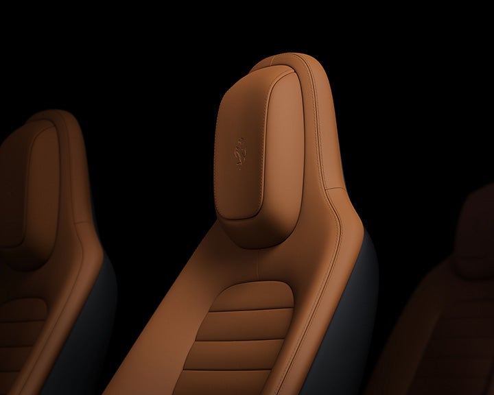 Close-up of a brown leather car seat with an embossed logo on the headrest, dark background.