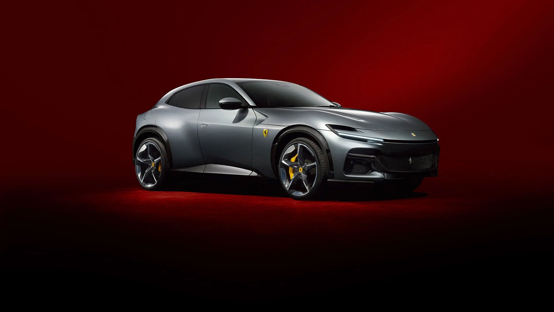 A gray Ferrari Purosangue parked on a reflective surface against a clear blue sky, overlooking a body of water.
