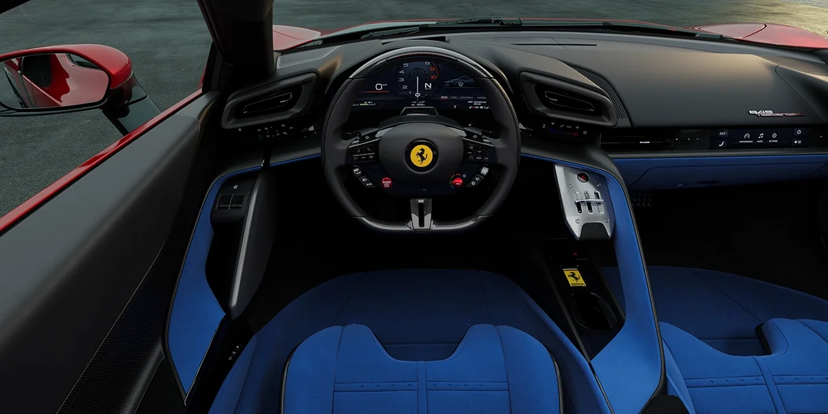 Driver’s cockpit view of the Ferrari 849 Testarossa featuring a sporty steering wheel, digital display, and blue seat upholstery.